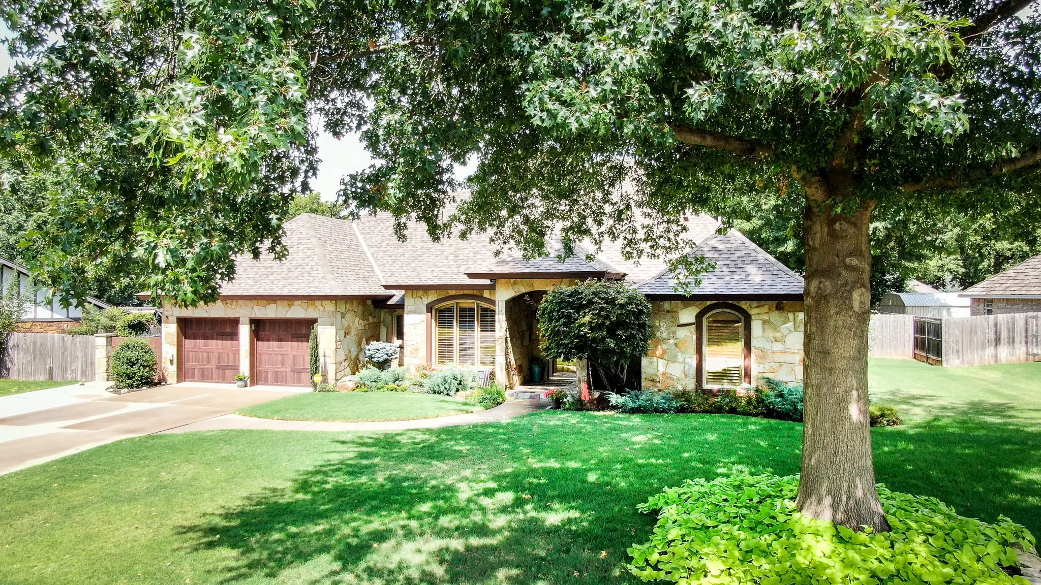 Stone ranch home with a two-car garage and a large shade tree
